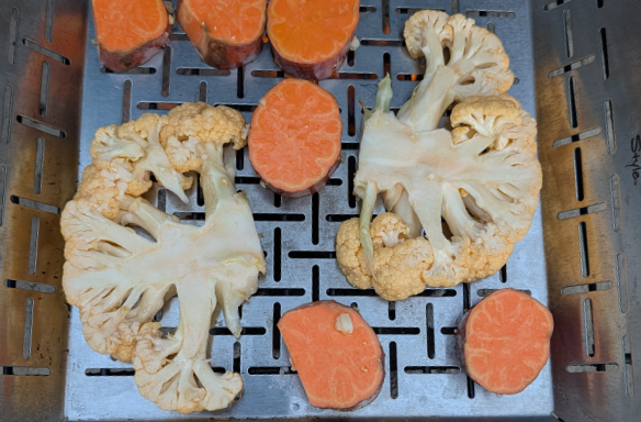 Cauliflower and sweet potato in a veggie basket grilling on the barbecue